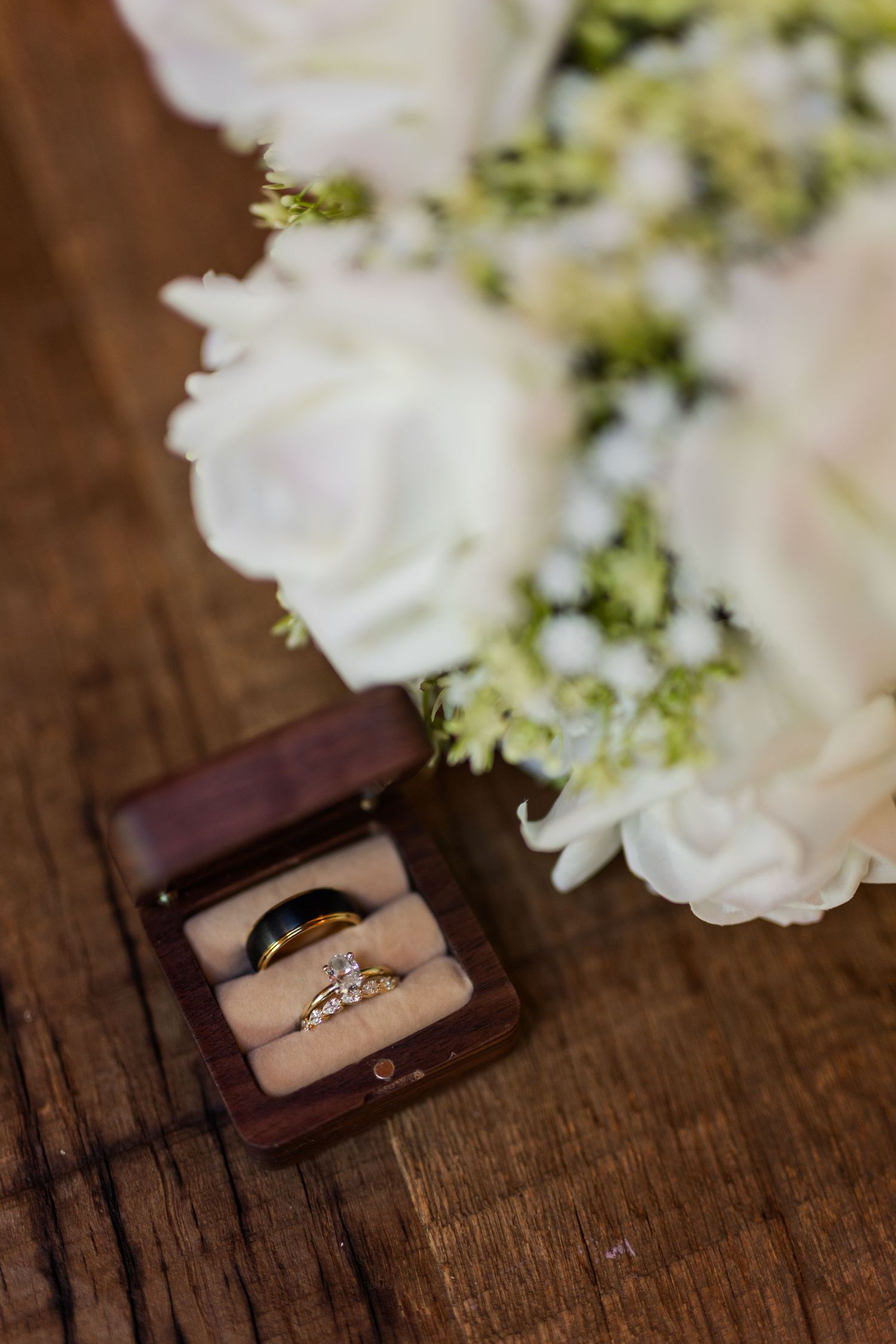 Elegant diamond engagement ring in brown leather box with white flowers on rustic wooden surface.