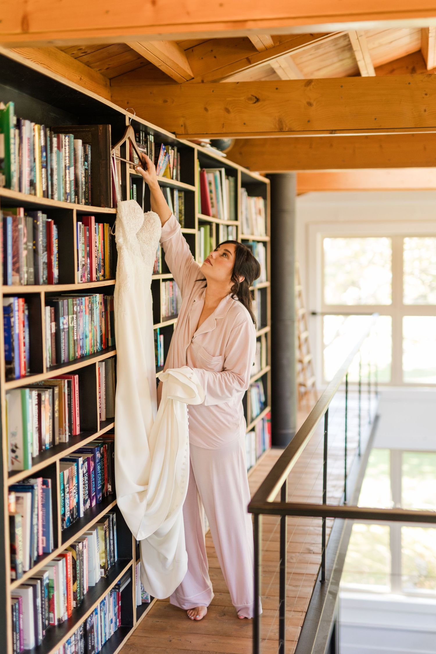 A figure in white flowing clothing stretches gracefully against wooden bookshelves in a sunlit library space.
