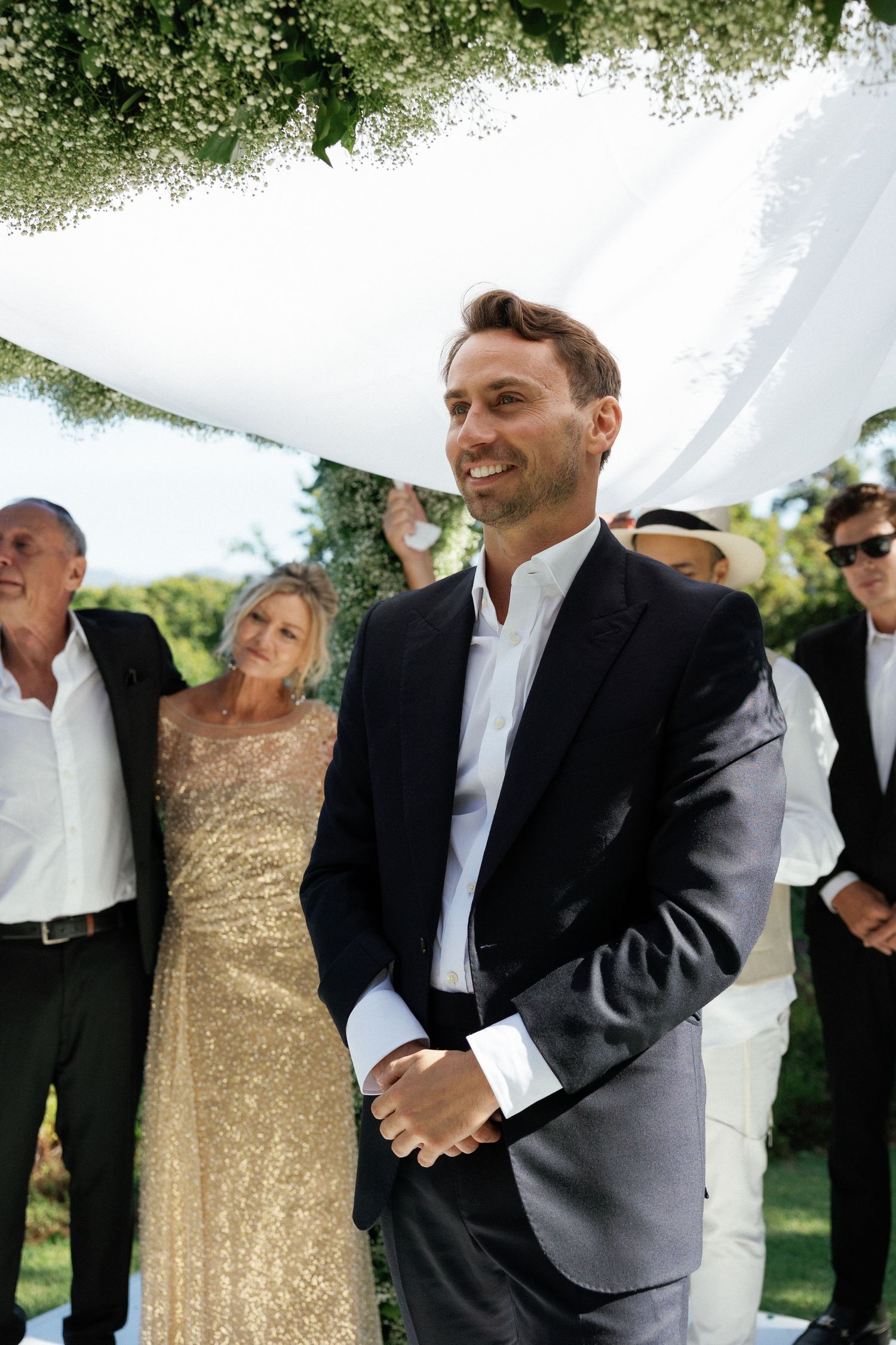 Wedding guests gather under a white tent canopy with greenery decorations during an outdoor celebration.