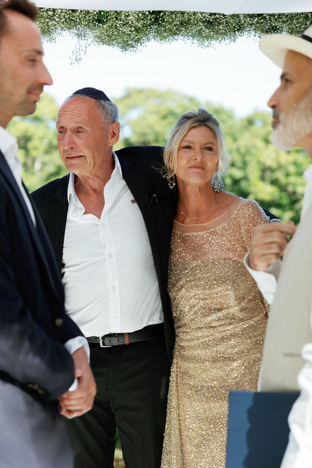 A couple shares a joyful moment at an outdoor event, with the woman wearing a sparkly gold dress.