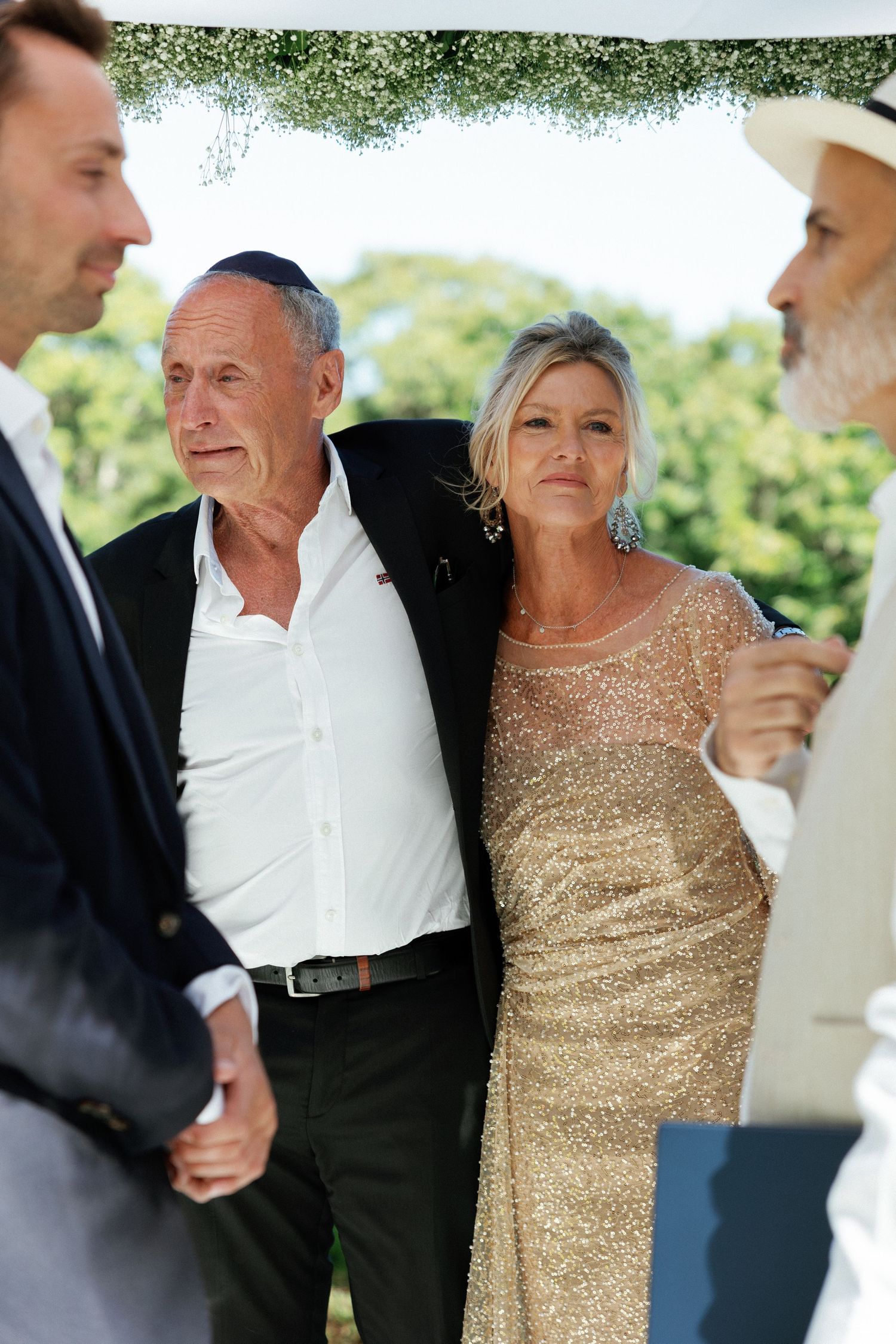 A couple shares a joyful moment at an outdoor event, with the woman wearing a sparkly gold dress.