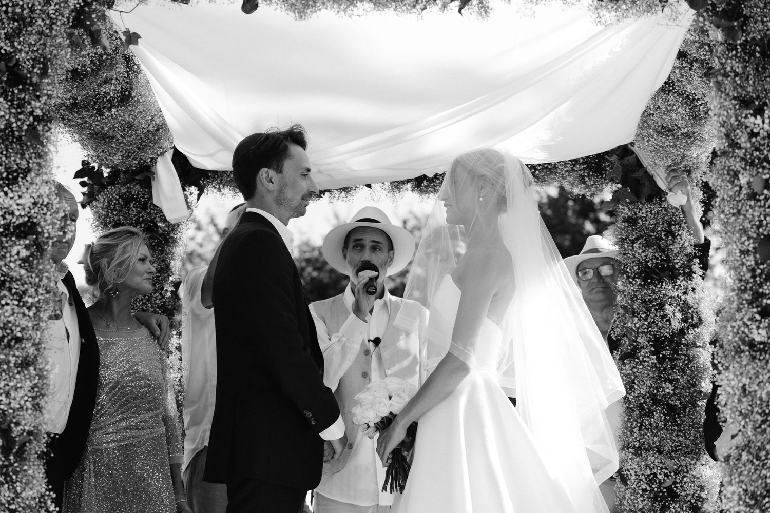 Black and white wedding photographs arranged in a filmstrip style showing romantic moments under a floral canopy.