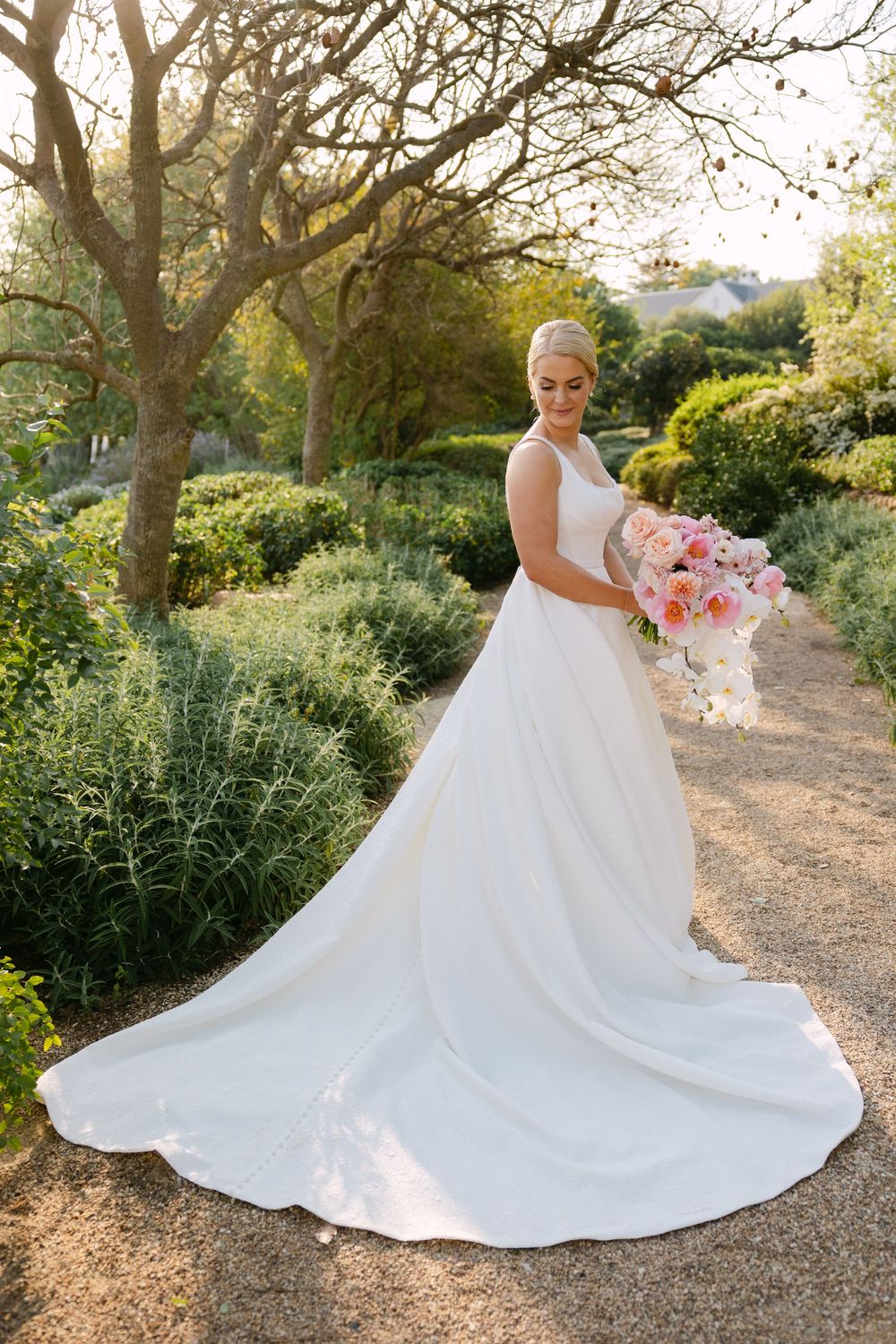 A stunning wedding dress with a flowing train is showcased in a garden setting during golden hour.
