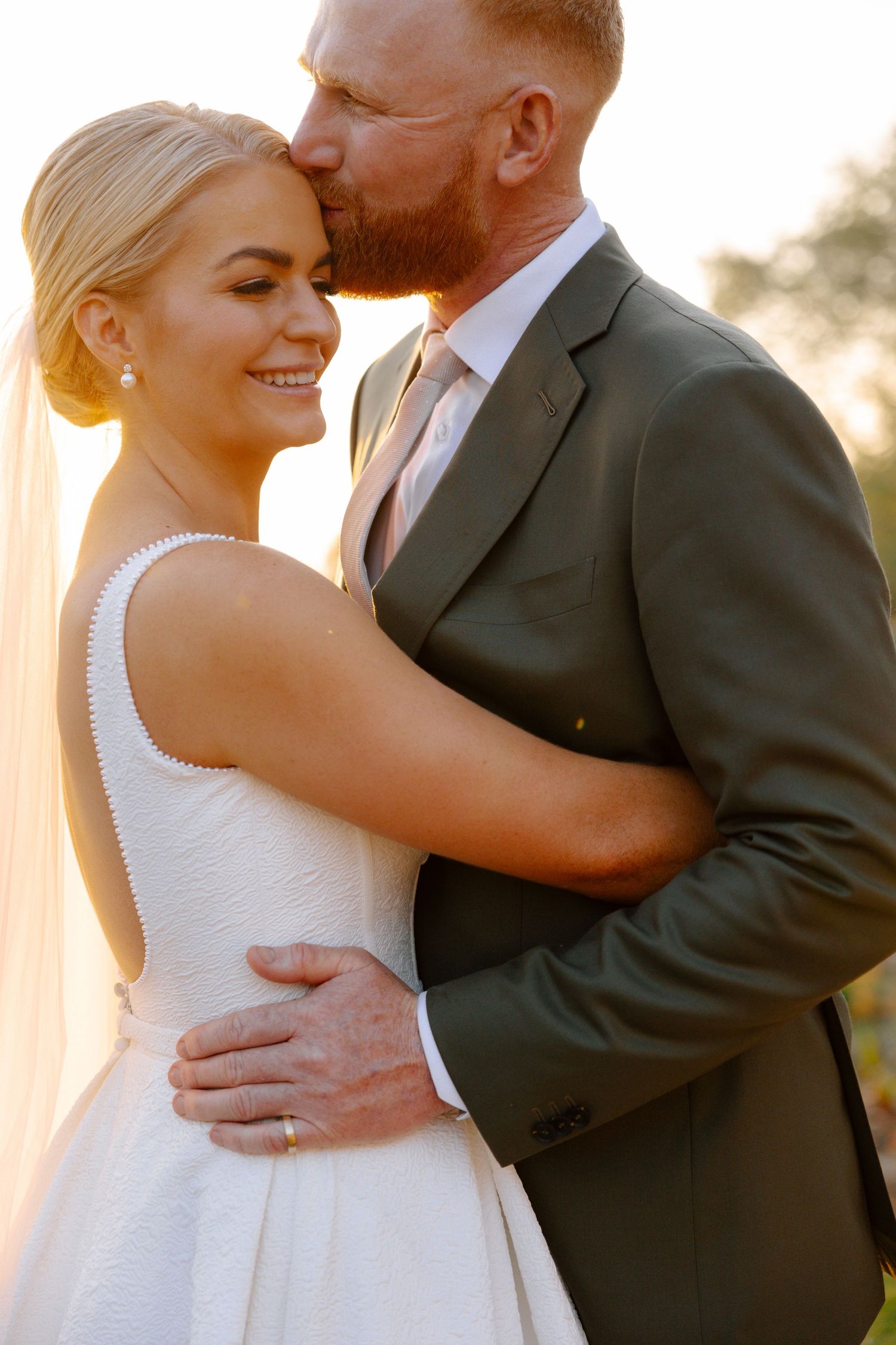 A romantic wedding couple embraces in golden sunlight during an intimate outdoor portrait session.