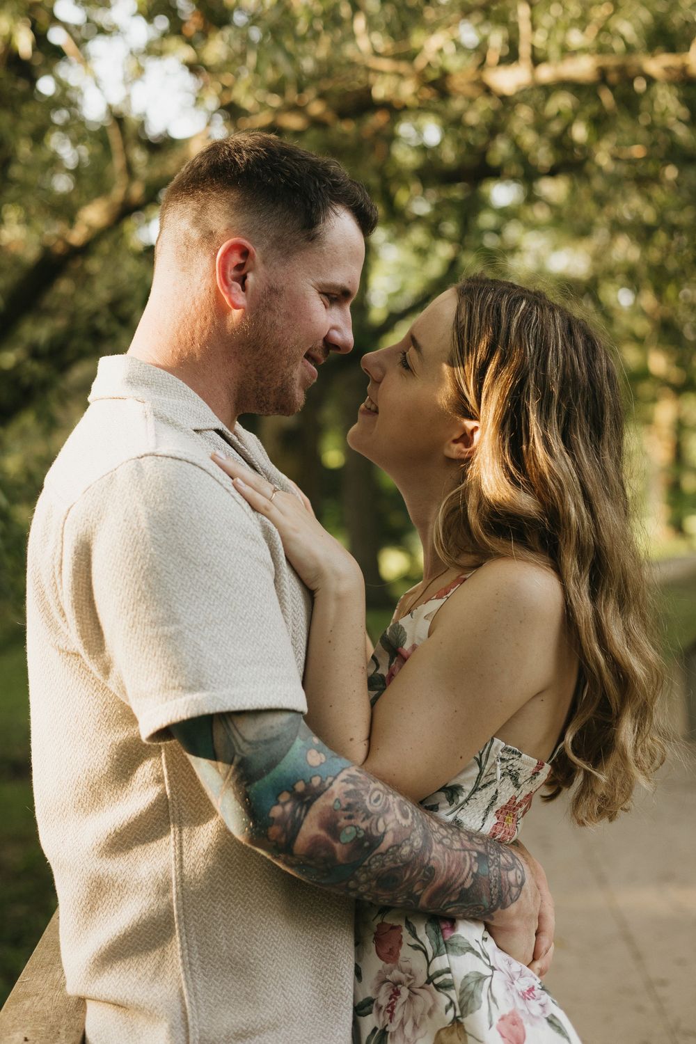 A romantic couple embraces in golden sunlight during a sunset photo session in a park setting.