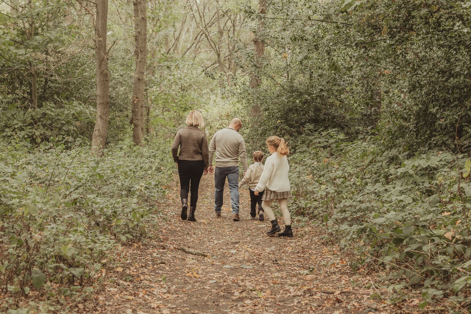 Three people walk together on a peaceful forest trail surrounded by lush green foliage on a misty day.
