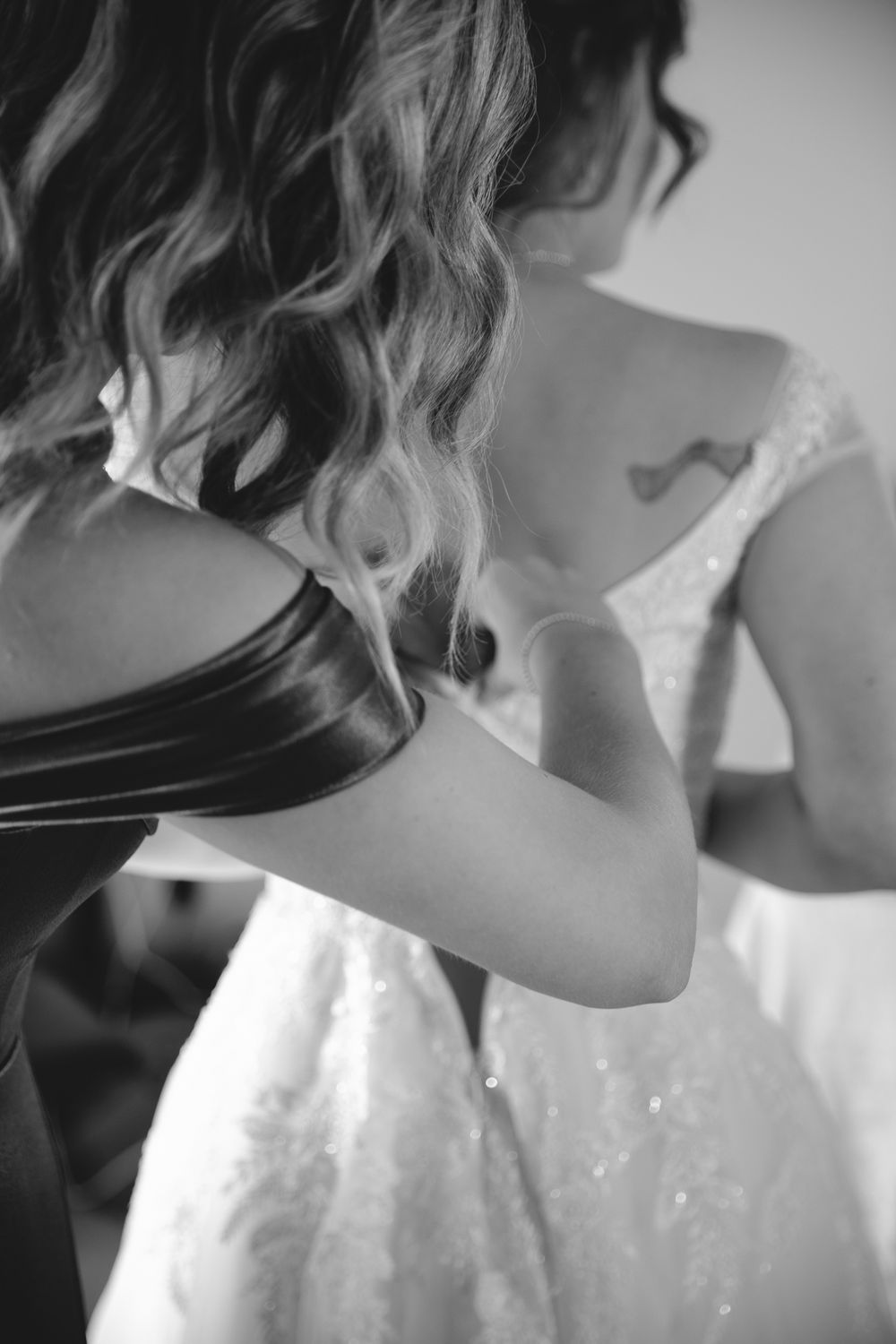A bridesmaid zipping up a brides dress on her wedding day in Vancouver, B.C., taken by Kristina Harnett.