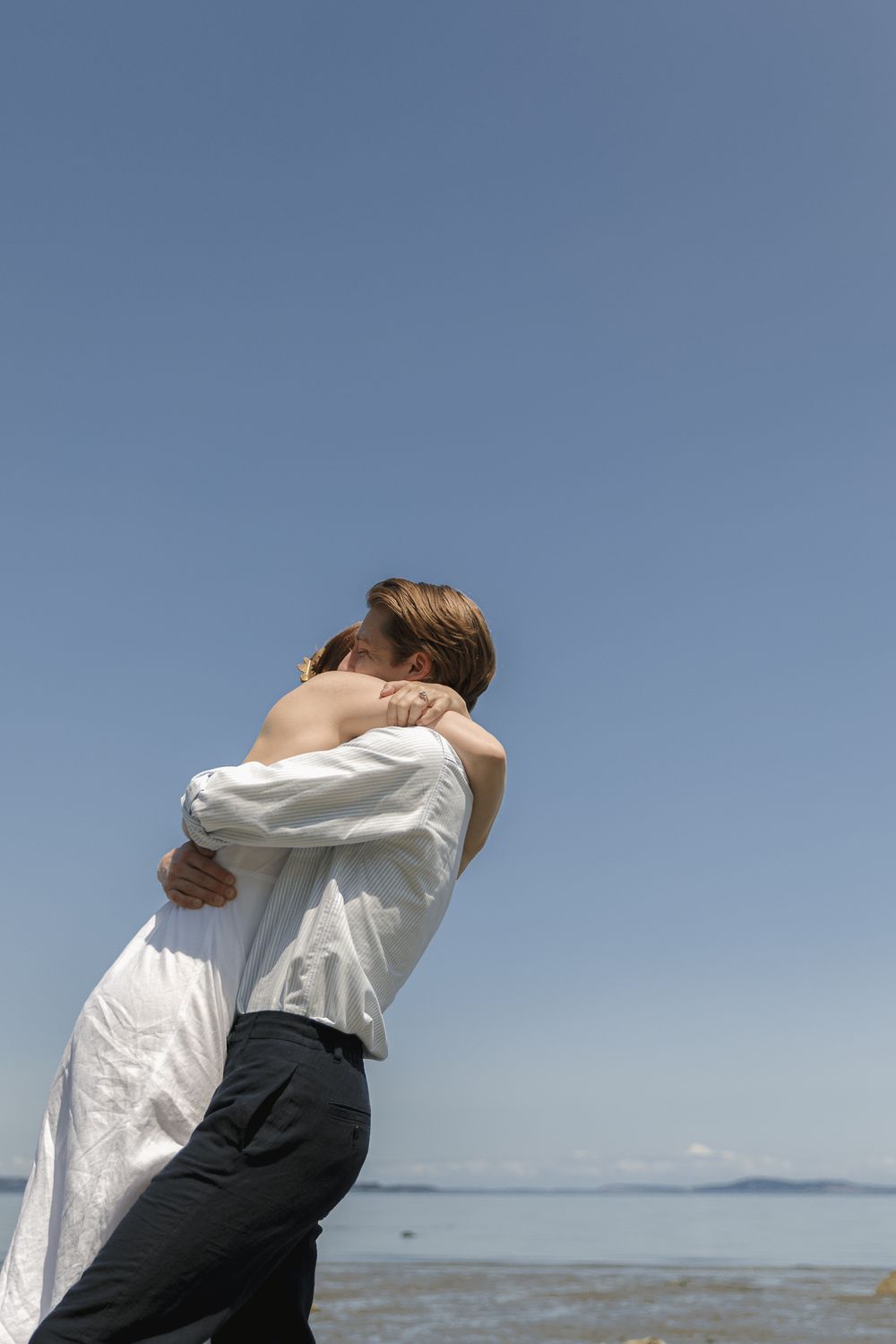 A couple giving each other a big hug on the beach during a Vancouver Island engagement session, taken by Kristina Harnett.