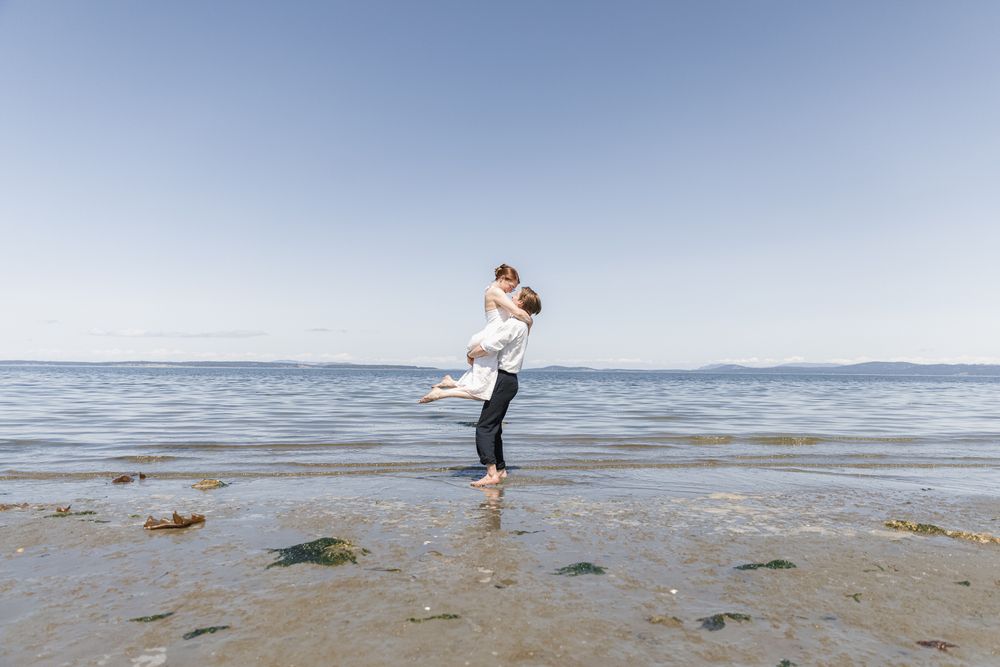 A couple doing a lift and spin on a Vancouver Island beach during an engagement session, taken by Kristina Harnett.