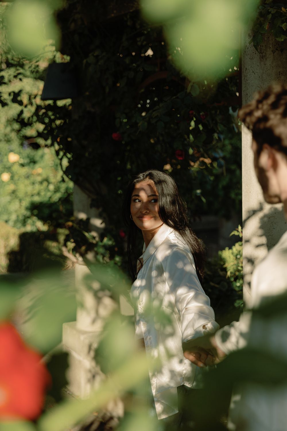 A woman leading her fiance through a garden at a Vancouver engagement session, taken by Kristina Harnett.