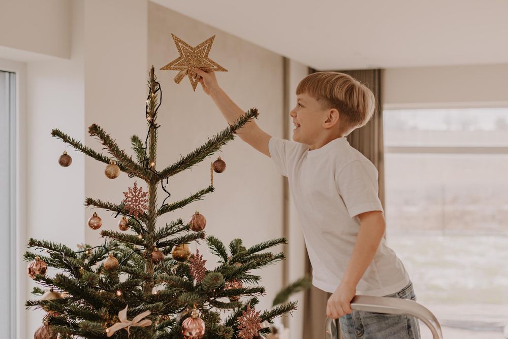 Two people decorating a fresh evergreen Christmas tree with ornaments in a bright modern living room.