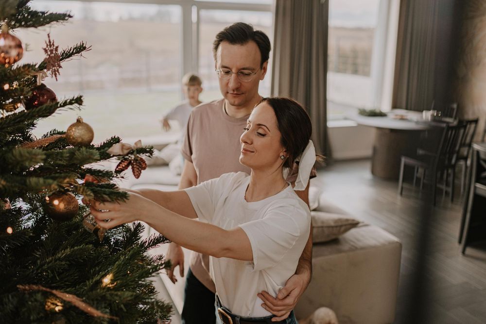 Two people decorating a Christmas tree together in a cozy living room with warm lighting.