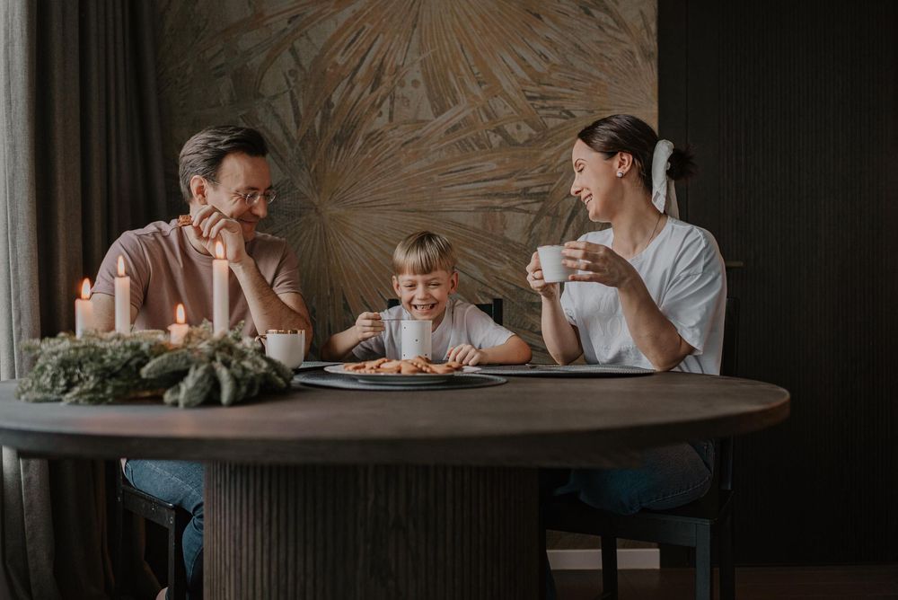 A family gathers around a wooden dining table sharing a meal together in warm lighting.