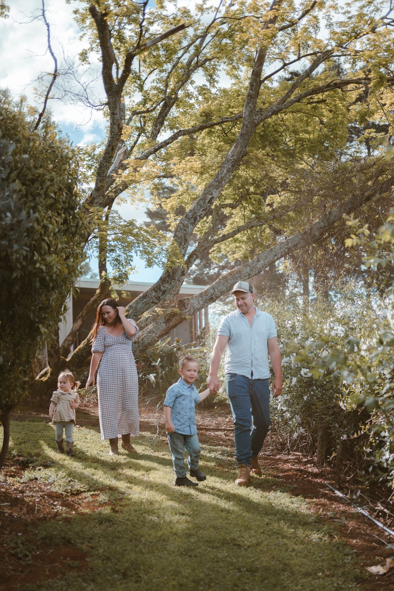 Family walking together down a sunlit hill among trees and natural landscaping.