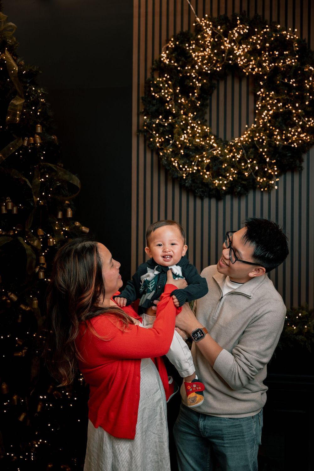 Family shares playful moment together in front of Christmas lights and decorations in dimly lit setting.