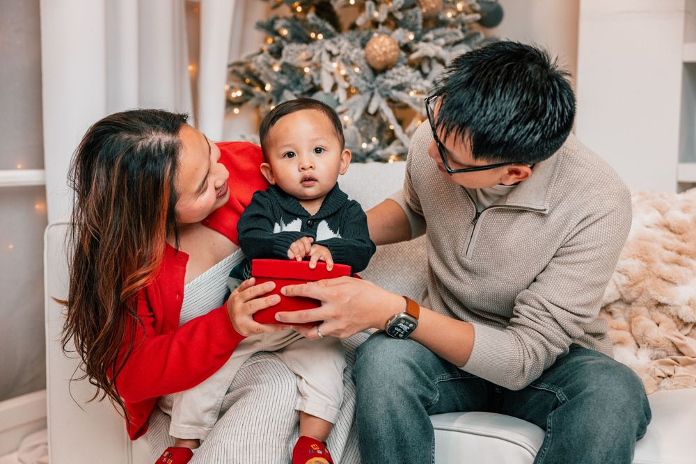 A family in matching red and gray outfits poses together on a couch during a holiday photo session.