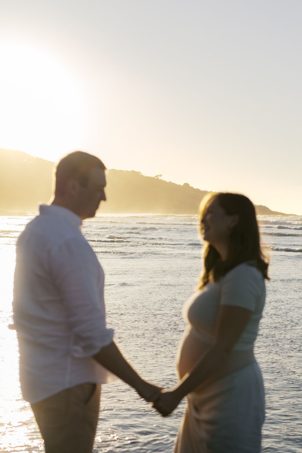 A couple holds hands on a sunset beach with mountains in the background creating a romantic silhouette.