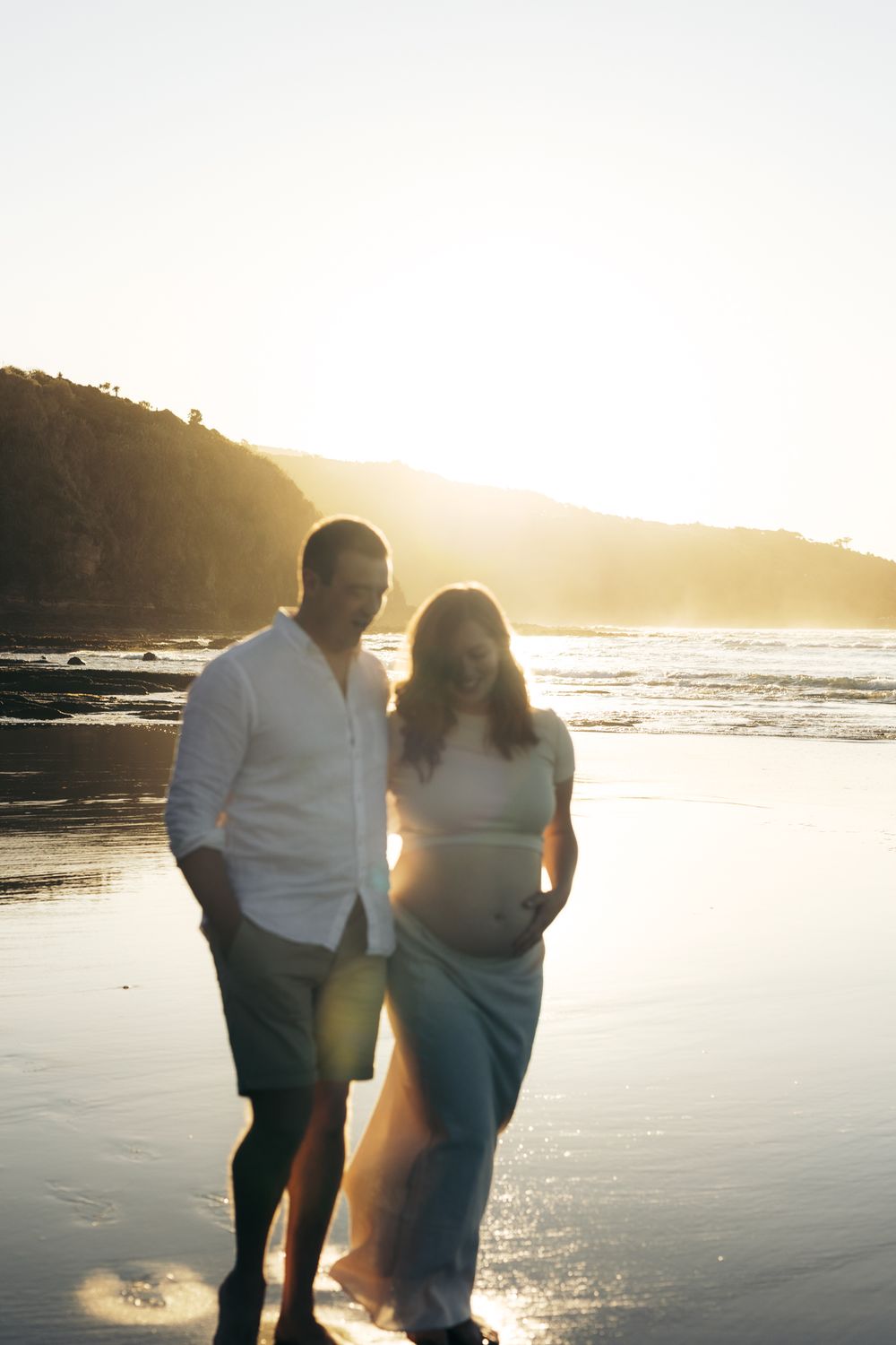 A couple walks along a sunlit beach at golden hour creating silhouettes against the glistening ocean waves.