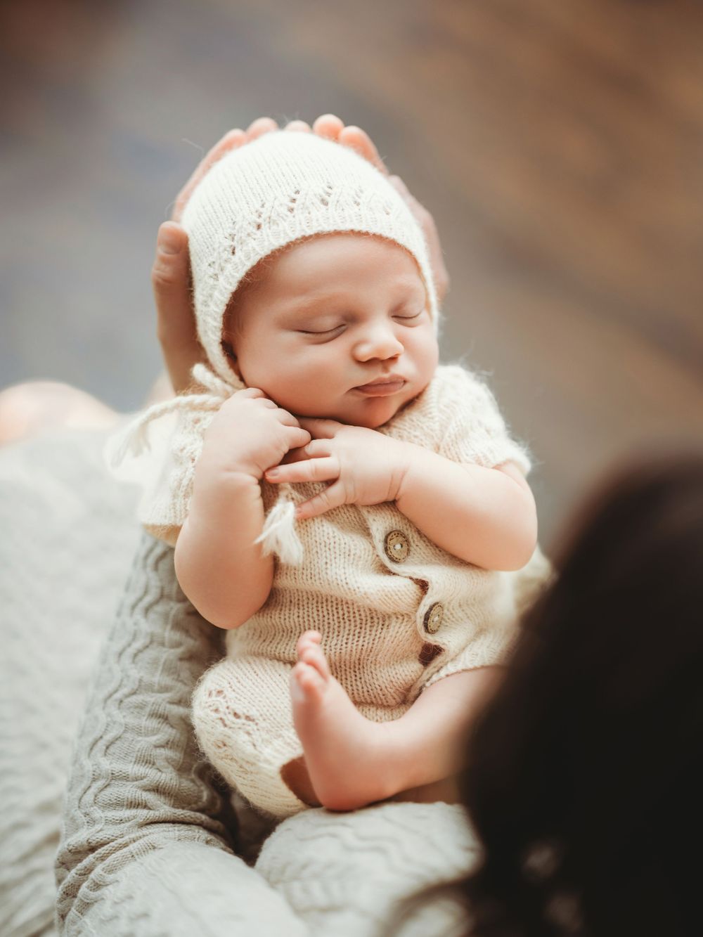 Newborn baby wearing soft knit cream-colored outfit sleeping peacefully on textured blanket.
