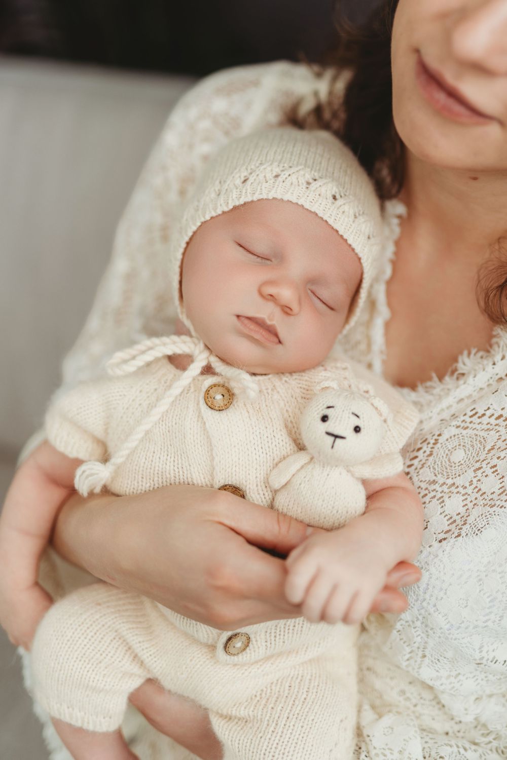 A peaceful baby in white knitwear cuddles a small plush bunny while nestled in delicate lace.