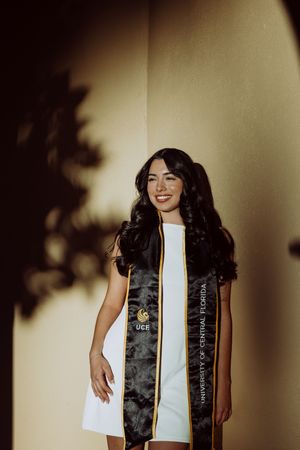 Graduate wearing black graduation stole smiles in indoor portrait session.