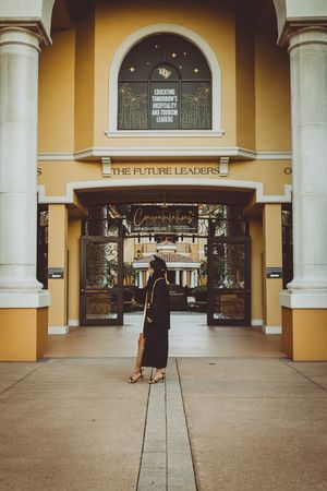 Figure in graduation attire stands in front of a store entrance with ornate columns and archways.