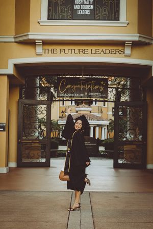 Graduation photoshoot in front of building with 'The Future Leaders' sign and yellow walls.