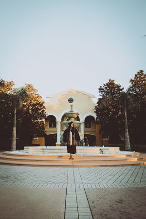 Wide panoramic view of a plaza with fountain and colonial-style architecture at sunset.