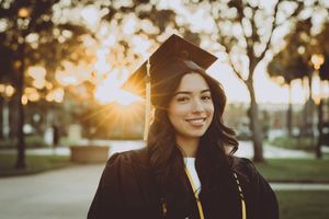 Graduate celebrates with cap against sunset sky on graduation day.