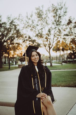Outdoor graduation photoshoot at sunset with black gown and gold honors cords.
