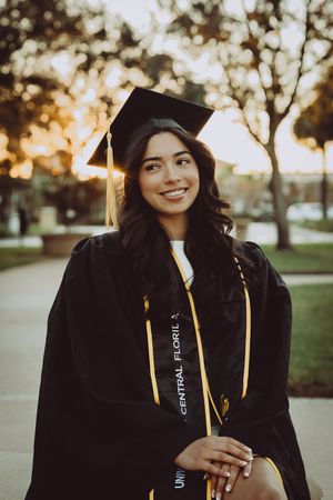 Graduate in black cap and gown smiling during golden hour sunset on campus.
