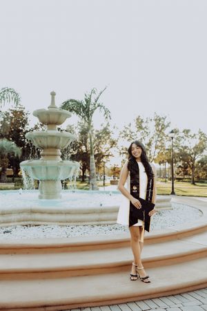 Graduation photo taken by ornate tiered fountain in a landscaped garden setting.