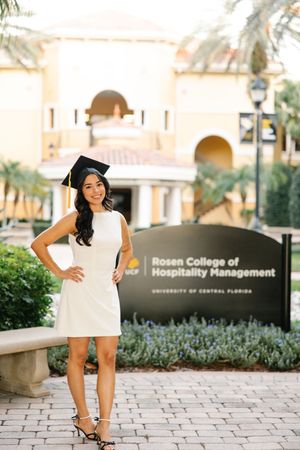 Graduate posing in front of Rosen College of Hospitality Management sign at UCF.