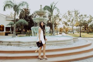 Wide shot of circular fountain with palm trees and graduate posing in outdoor setting.