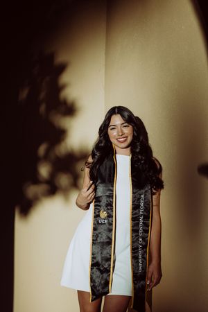 Graduate wearing graduation stole poses against warm-toned wall.