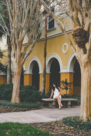 Graduate walks along covered walkway with yellow walls and white arches.