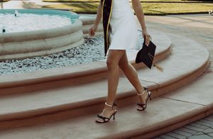 White dress and strappy heels walking on curved stone steps near a fountain.