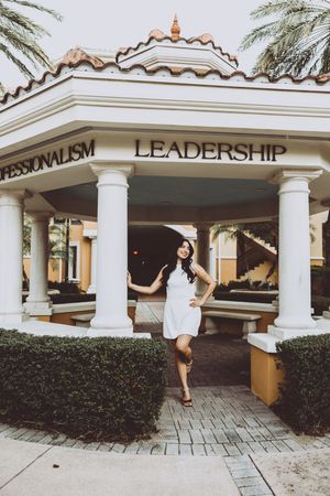 Graduate poses playfully in front of leadership building with columns.