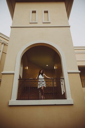 Graduate poses on balcony of Mediterranean-style building at sunset.