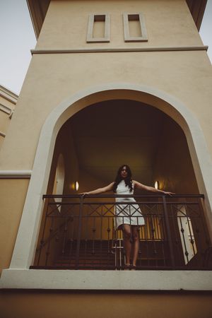 Graduate poses on balcony of Spanish colonial style building with arched architecture.