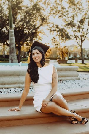 Graduate in white dress sitting on stone steps during golden hour photoshoot.