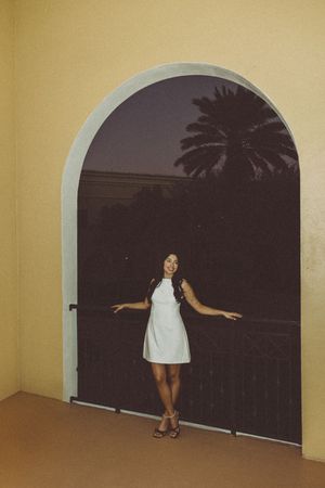 A figure in white clothing strikes playful poses on a balcony against a dark evening sky.