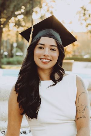 Graduate in cap and white dress smiles in golden sunset light.