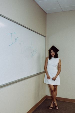 Graduate in white dress and cap stands by whiteboard showing progression of poses.
