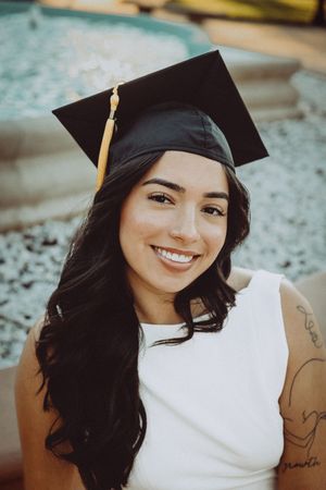 Close-up graduation portrait showing cap, tassel and white dress against blurred background.