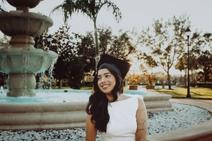 Graduate poses by outdoor fountain during golden hour.