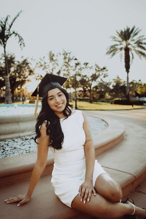 Casual graduation photo series taken at sunset with palm trees and a curved stone wall.