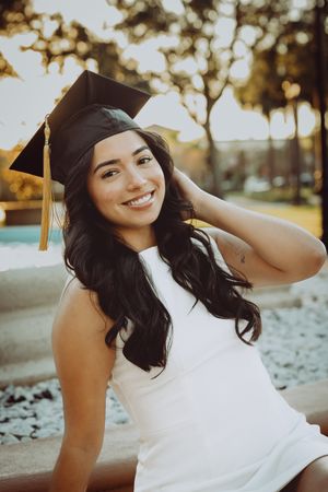 Graduate in cap and gown smiles joyfully during outdoor graduation photoshoot.