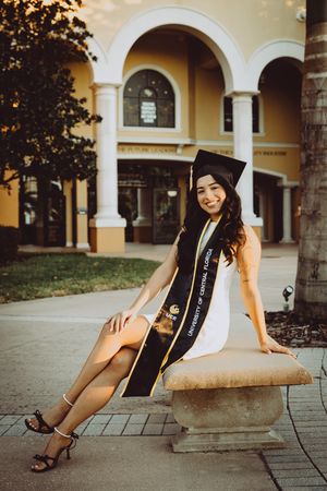 Graduate wearing sash and cap reclines on stone bench near Mediterranean-style columns and archways.