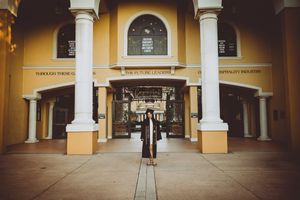 Graduate stands in front of yellow building with white columns and arched entrance.